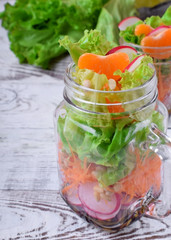 Layered salad in a jar with mandarins, radish, lettuce leaves, carrot and dressing