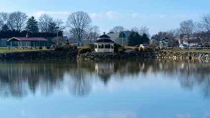 Fototapeta na wymiar A small pond with a gazebo reflecting in the water, on a beautiful, calm and quiet day, Lancaster County, PA
