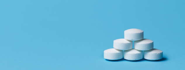 Heap of white pills on blue background. Medical, pharmacy and healthcare concept.