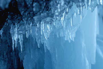 view from  ice cave. frozen, crystal clear water drops like stalactites hang from the ceiling. rising sun stained ice. partially tinted photo. focus on a central object. Extra shallow depth of field.