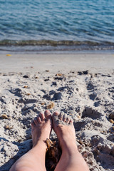 Woman feet in the sand with a blue sea water on a background on corsican beach. France 2019.