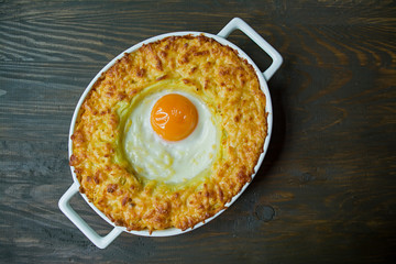 Potato casserole with bolognese. Baked potato casserole with egg and grated cheese in a ceramic oval baking sheet. Wooden dark background.