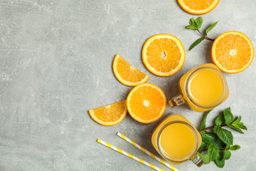 Flat lay composition with orange pieces, mint, tubules and glass jars with fresh orange juice on grey background, space for text. Fresh natural drinks