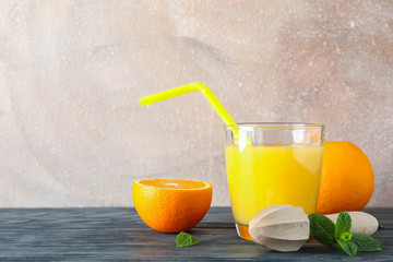 Glass with fresh orange juice and tubule, oranges, mint and wooden juicer on wooden table against...