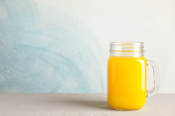 Glass jar with fresh orange juice on white table against color background, space for text. Fresh natural drink