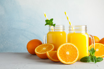 Glass jars with fresh orange juice and tubule, oranges and mint on white table against color background, space for text. Fresh natural drink