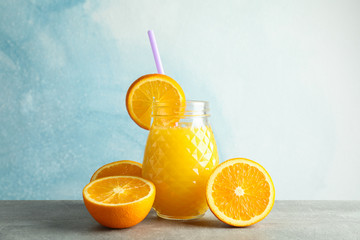 Obraz na płótnie Canvas Glass jar with fresh orange juice, tubule and oranges on grey table against color background, space for text. Fresh natural drink