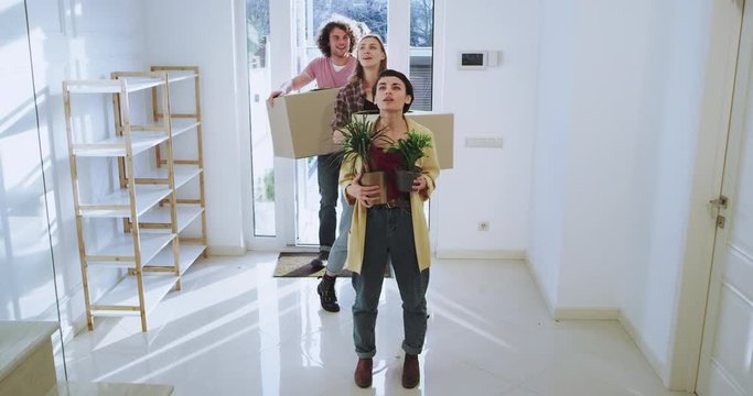 Charismatic and attractive couple and their friends moving to a new house very impressed and excited they holding big boxes and flowers, modern house interior