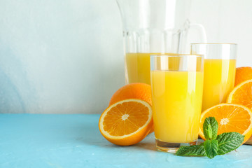 Composition with fresh orange juice in glassware, mint and wooden juicer on color table against white background, space for text. Fresh natural drink