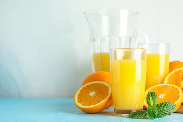 Fototapeta na wymiar Composition with fresh orange juice in glassware, mint and wooden juicer on color table against white background, space for text. Fresh natural drink