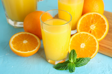 Composition with fresh orange juice in glassware, mint, and oranges on color background, closeup. Fresh natural drink