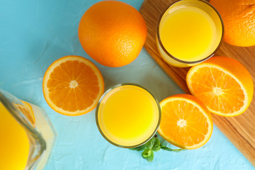 Composition with fresh orange juice in glassware, mint, and cutting board with oranges on color...