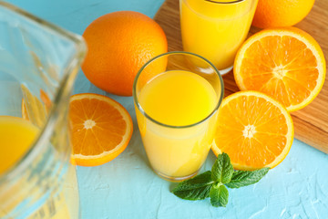 Composition with fresh orange juice in glassware, mint, and cutting board with oranges on color...
