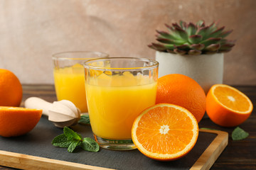 Obraz na płótnie Canvas Cutting board, orange juice, wooden juicer, mint, orange, tubule and succulent plant on wooden table, space for text. Fresh natural drink and fruits