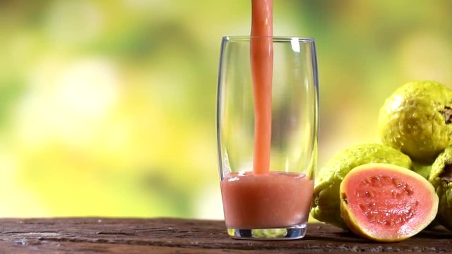 Red guava juice pouring in a glass with tree blurry background . Preparing juice. Slow motion.