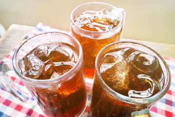 Three glasses of cola with ice on table cloth.