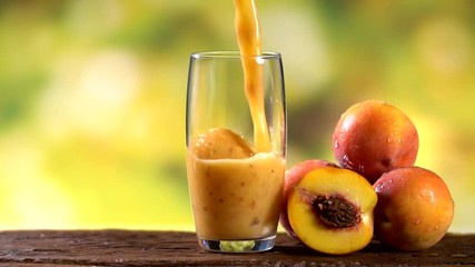 Peaches juice pouring in a glass with tree blurry background . Preparing juice. Slow motion. - Powered by Adobe