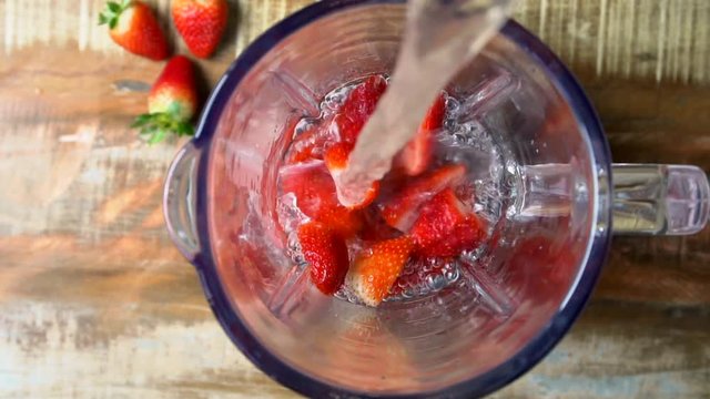water pouring in a blender with strawberry. Juice preparing. Slow motion, top view