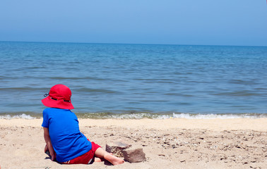Funny kid boy resting on sand beach by the sea . Young child enjoying summer vacation. Place for your text.