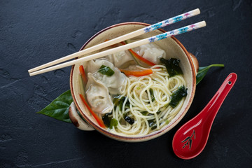 Bowl of chinese noodle soup with wontons on a black stone background, high angle view
