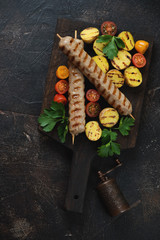 Grilled chicken skewers with fried mini potato and cherry tomatoes, above view on a dark brown stone background