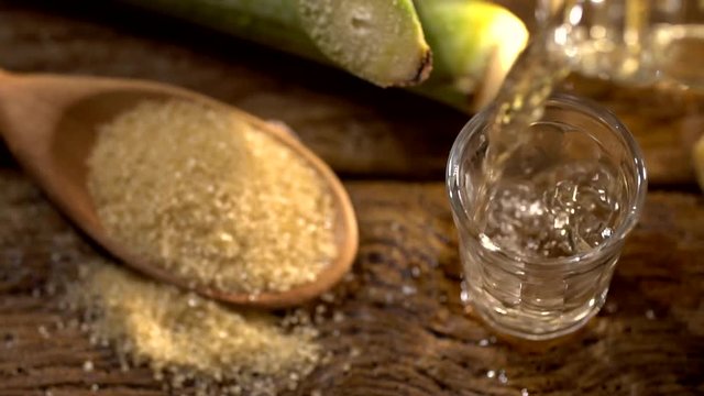 Brazilian gold cachaca pouring in glass cup. Sugar Cane Derivatives. Sugar and sugarcane on old wood background.