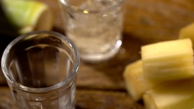 Brazilian gold cachaca pouring in glass cup. Sugar Cane Derivatives. Sugar and sugarcane on old wood background.