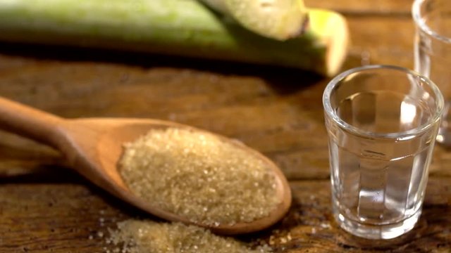 Brazilian gold cachaca pouring in glass cup. Sugar Cane Derivatives. Sugar and sugarcane on old wood background.