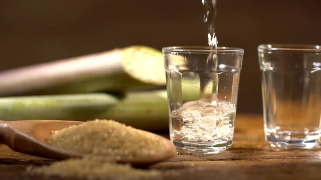 Brazilian gold cachaca pouring in glass cup. Sugar Cane Derivatives. Sugar and sugarcane on old wood background.
