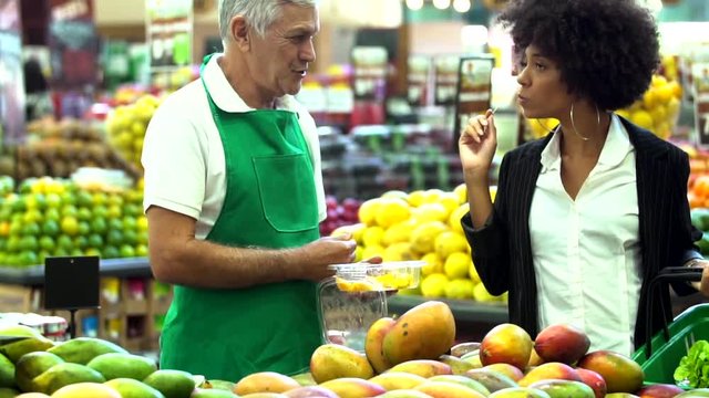 Shop assistant holding fruit with african woman customer in the supermarket 