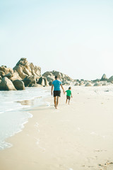 happy family on beach playing, father with son walking sea coast, rocks behind smiling taking vacation