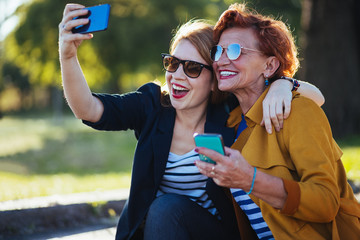 Mature mother and adult daughter taking selfie in the park