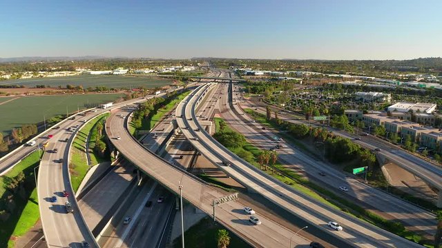 Aerial view or drone shot from above over a busy freeway overpass or interstate with cars rushing below on a blue sky day.