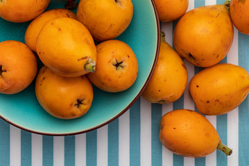 Fresh loquats (medlars) in blue turquoise bowl. Rustic and healthy appearance. Close-up.Top view.