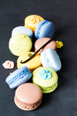 Multicolored french macaroon cookies with vanilla stick on a dark background