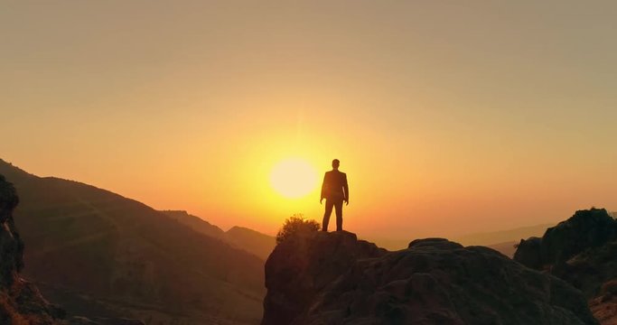 successful businessman standing on top of a mountain, victoriously raising his hands up - way to success, on top of world concept 4k aerial