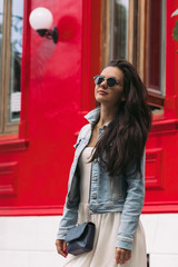 attractive woman in sunglasses and dress walks through the city streets on a sunny day. girl against a red wall