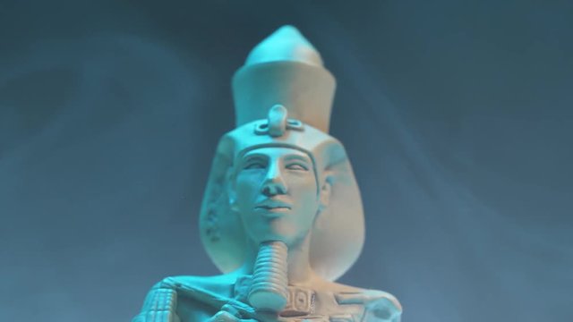 Dramatic shot of an Egyptian Nefertiti figure and smoke around.