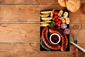 Grilled sausages with vegetables and spices in plate on wooden table. Close up macro top view.