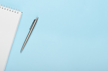 White notepad with metal pen on a blue background. Office, copy space, mock up, template, top view, flat lay.
