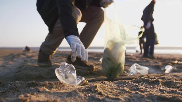 Close up shot of young man picking up plastic bottles on the beach, slow motion