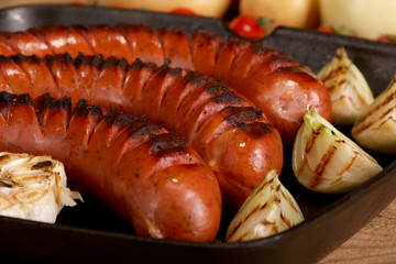 Grilled sausages with vegetables and spices in a pan on wooden background