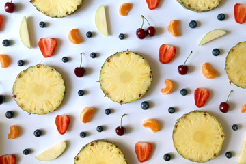 Various fruits and fruit slices on white background: pineapple,apple, strawberry, banana, blueberry, cherry and tangerine. Top view, flat lay.