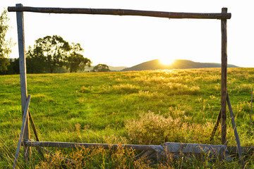 Beautiful scenery of green meadow during sunset above small hill. Wooden frame for playing soccer on a field.