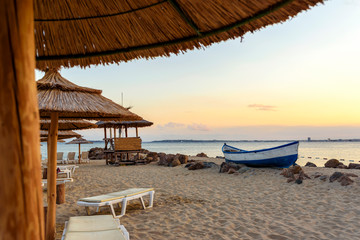 Relax evening in paradise resort. Sand beach, boat, sunbeds and umbrella with beautiful landscape. Summer seascape in sunset light.