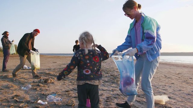 Little children helps their parents to clean up area of dirty beach with garbage bags