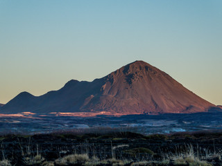 Fototapeta premium A tall mountain catching the first sun beams of the day, covered with soft light colors. The ground is still shrouded in darkness.