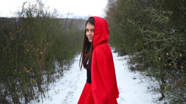 Fashion model woman in red riding costume walking down the snowy forest road while following me gesture.