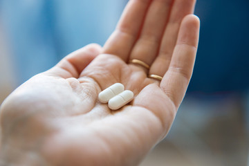 Close-up view of a hand holding two white pills in the palm above a blurry background, painkiller - obrazy, fototapety, plakaty