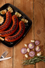 Grilled sausages with vegetables and spices in a pan on wooden background. Top view